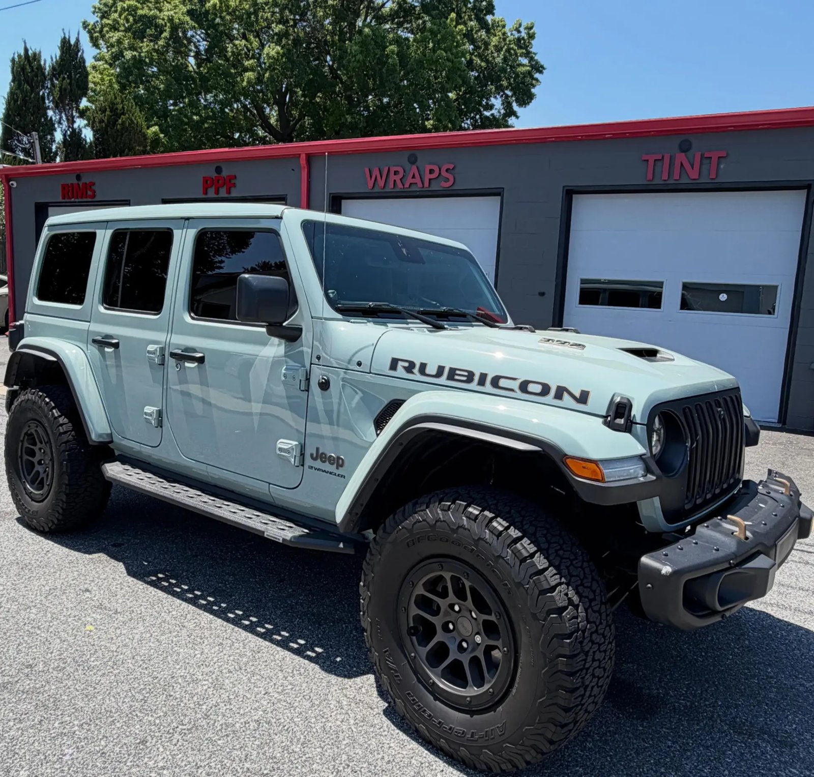 Light blue Jeep Wrangler Rubicon 392 with tinted windows in front of the shop's Rims, PPF, Wraps and Tint bays
