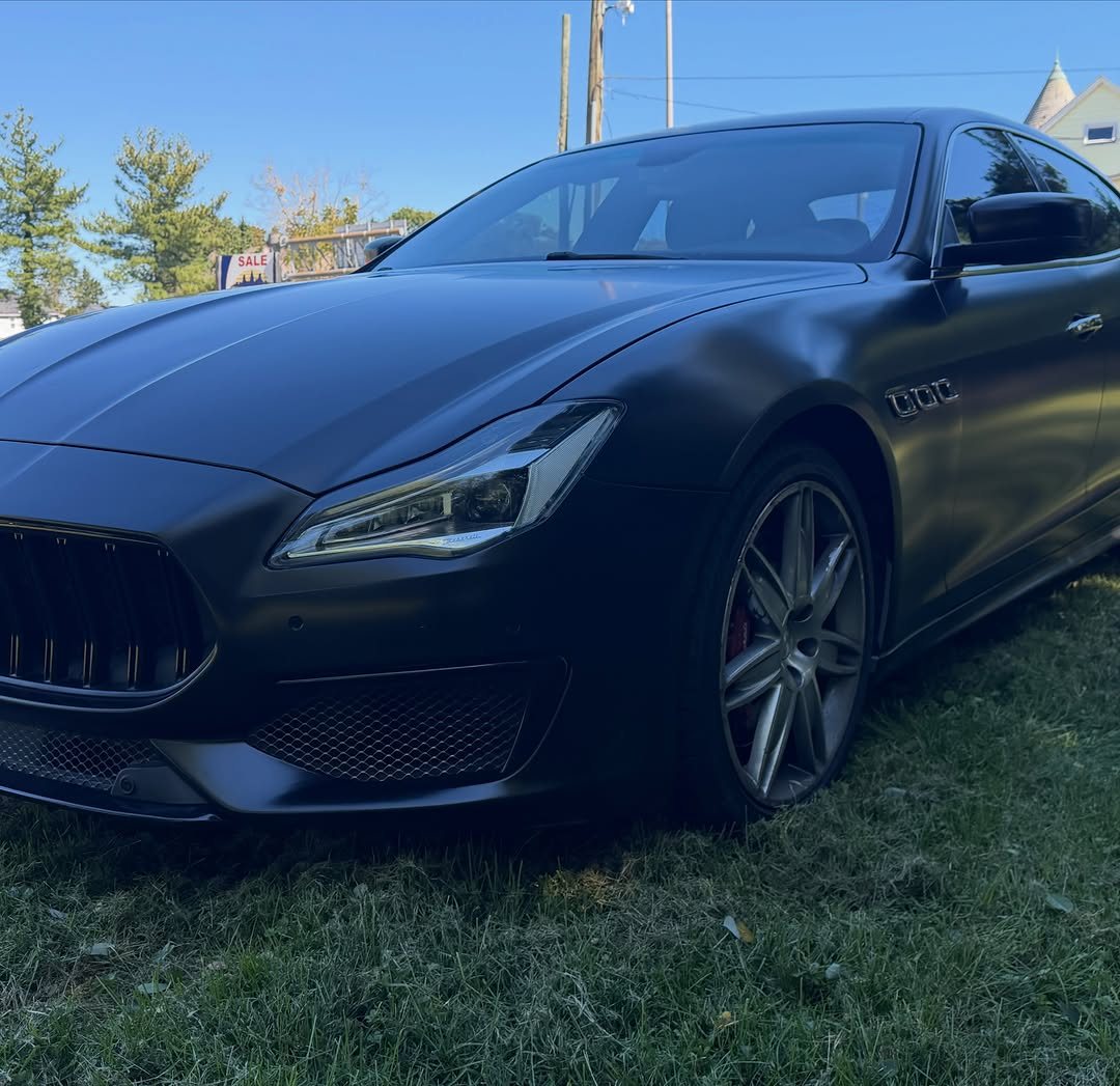 Maserati sedan in satin black wrap, front three-quarter view on grass