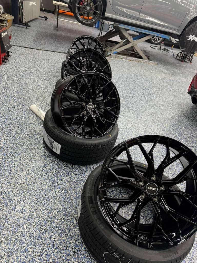 Set of gloss black aftermarket wheels with new tires in the shop