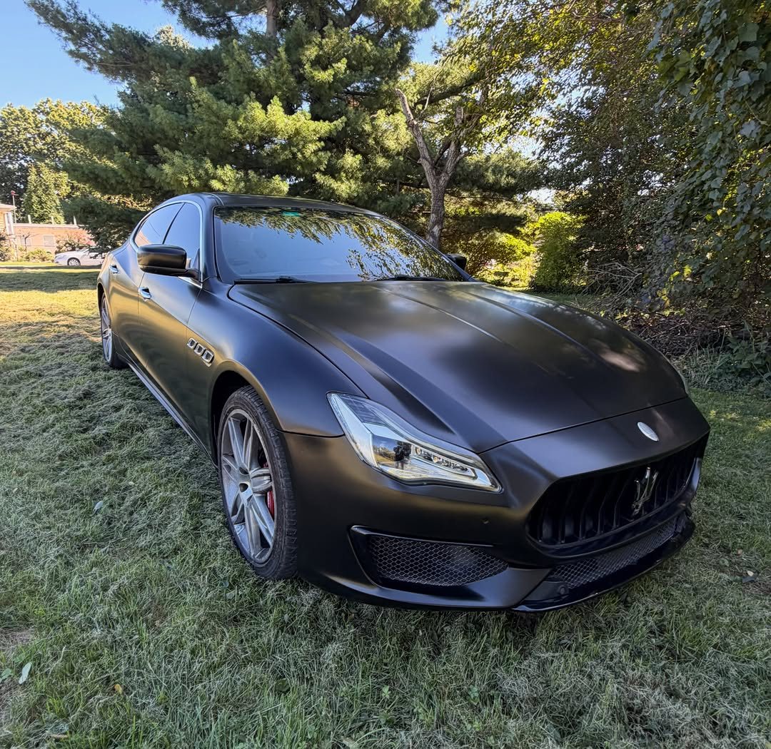 Maserati in satin black vinyl wrap, front three-quarter view on grass