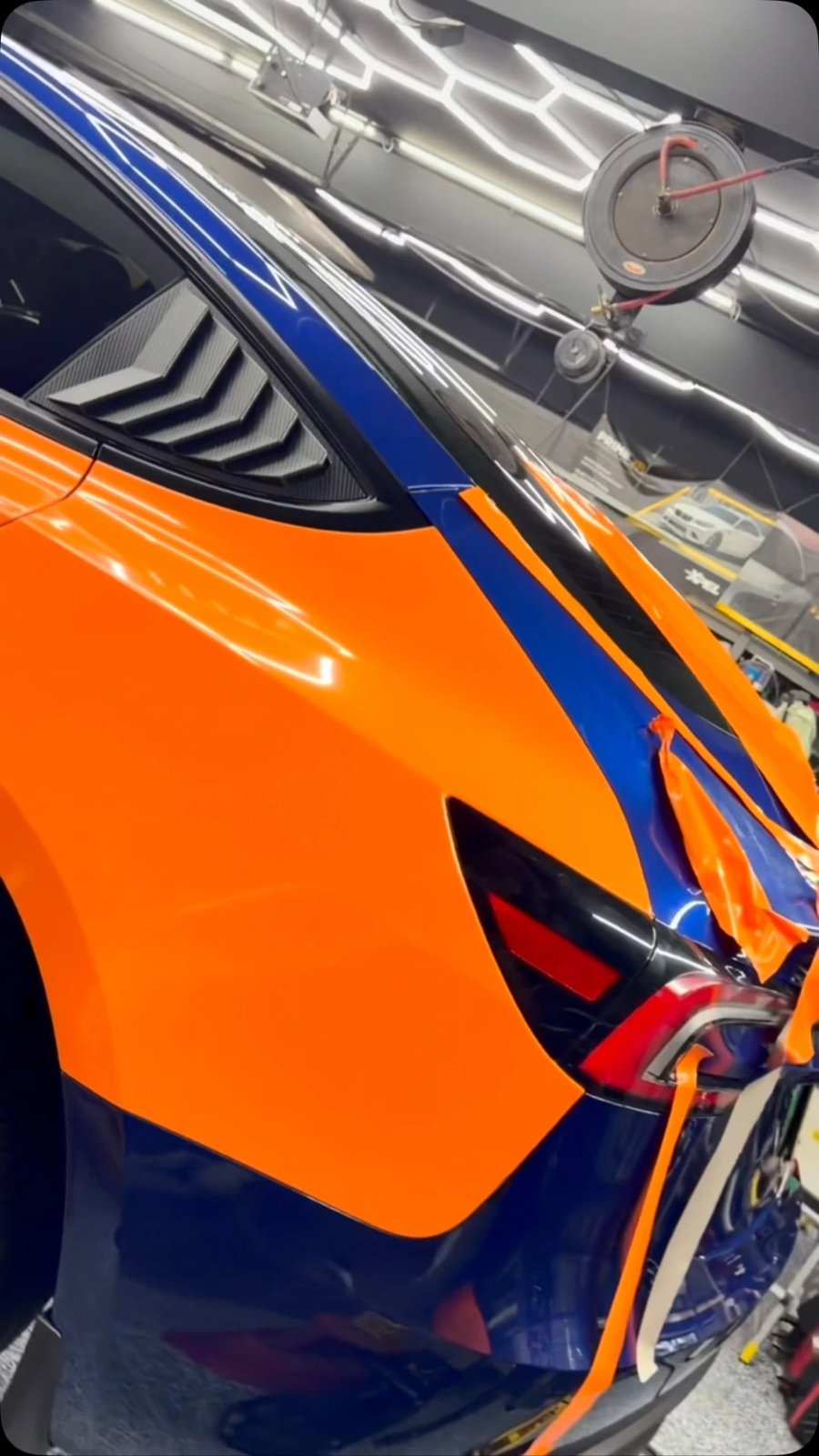 Close-up of gloss orange vinyl wrap being installed over blue paint in the shop