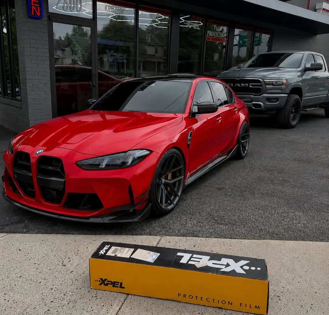 Red BMW M3 outside the shop with an XPEL paint protection film box on the curb