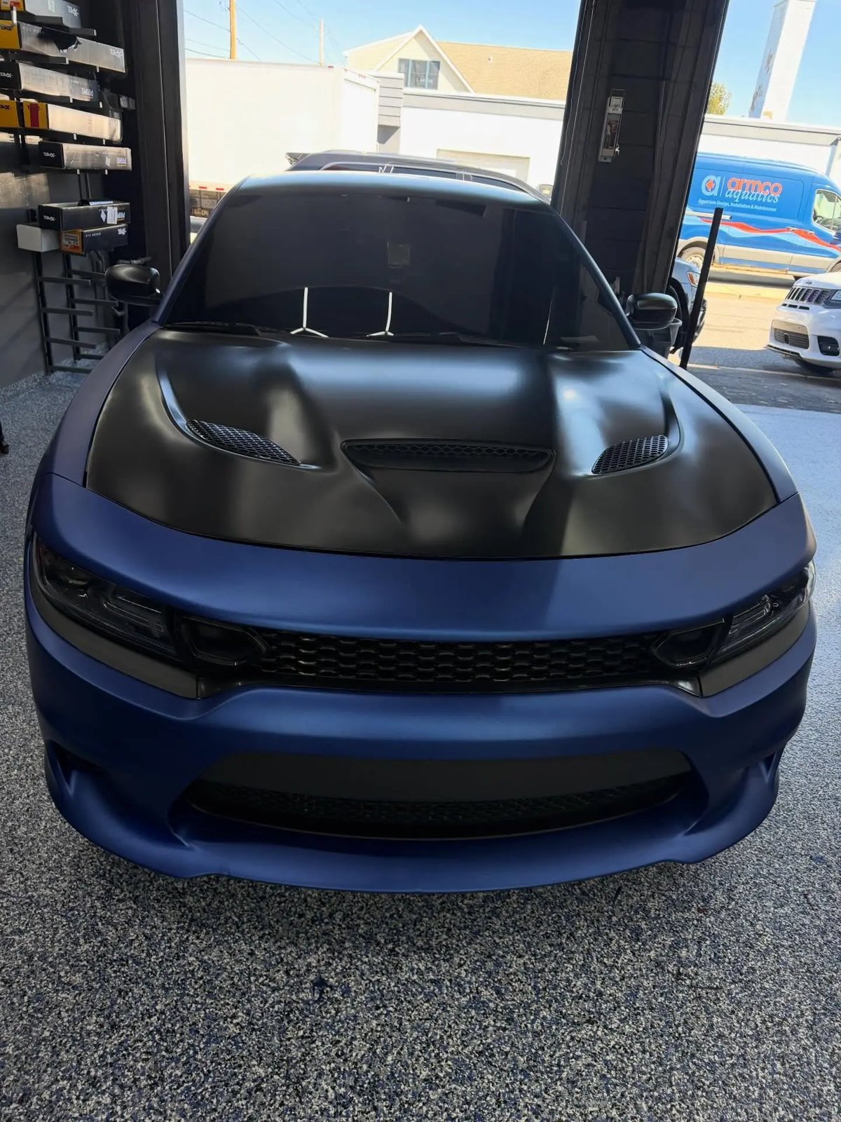 Dodge Charger in satin blue wrap with a black hood inside the shop bay