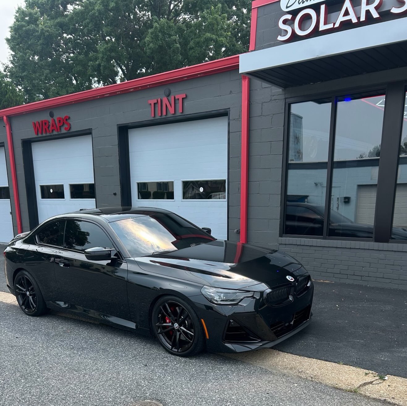 Black BMW coupe with tinted windows in front of the shop's Wraps and Tint bays
